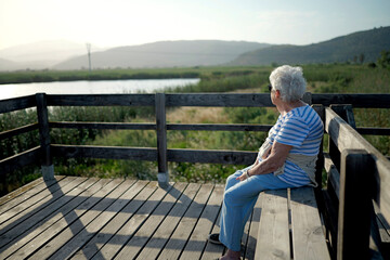 Fototapeta premium Healthy aging and senior lifestyle elderly woman sitting on a wooden bench enjoying nature and outdoor activity