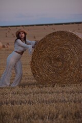 Young beautiful woman pushing huge round hay bale in harvested field⁠ © Даниел Маринов