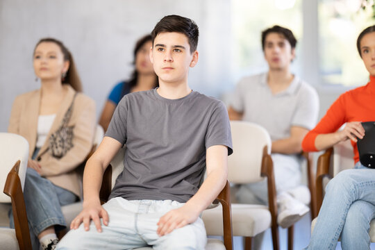 Focused young boy sitting and listening to lecture together with others in training room