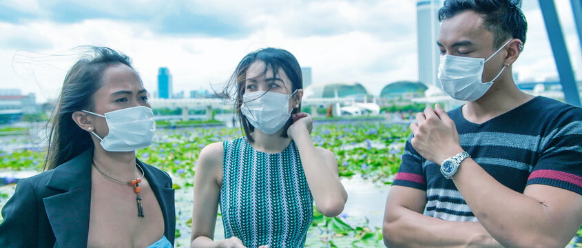 Three asian young friends standing outdoor in the city talking and wearing face masks in covid coronavirus pandemic