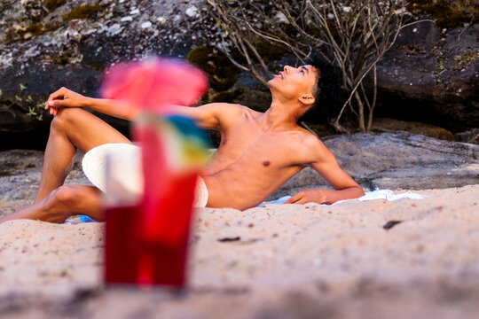 Young man relaxing on a sandy beach enjoying summer sun and a refreshing cocktail