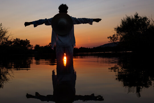 Man standing with arms outstretched on lake surface during summer sunset