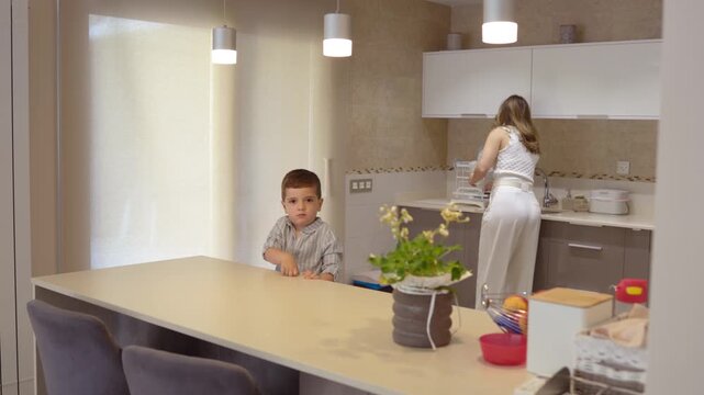 Mother preparing a baby bottle for her curious son in a modern kitchen