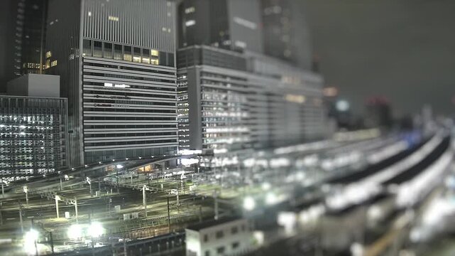 Night timelapse of illuminated railway lines and modern high rise buildings in Nagoya, Japan. Urban cityscape with lights and transportation infrastructure.