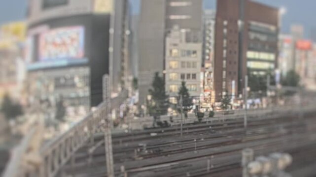 Timelapse of urban railway tracks and high rise buildings shifting from daytime to night lights in Tokyo Japan. Tilt shift miniature effect with glowing city signage.