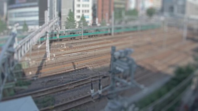 Timelapse view of multiple railway tracks as a commuter train passes through an urban corridor in Tokyo Japan. Tilt shift style blur creates a miniature city look.