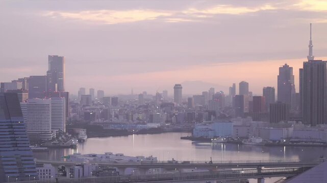 Timelapse of Tokyo waterfront skyline transitioning from night lights to colorful dawn and golden morning. High-rise buildings and reflections shimmer across the bay.