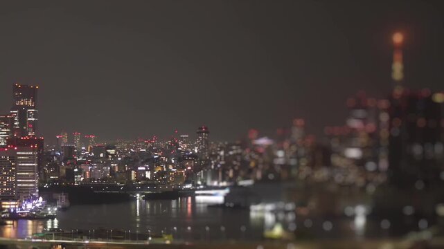 Night timelapse of Tokyo, Japan skyline with illuminated high rises and waterfront reflections, featuring soft bokeh in the foreground.