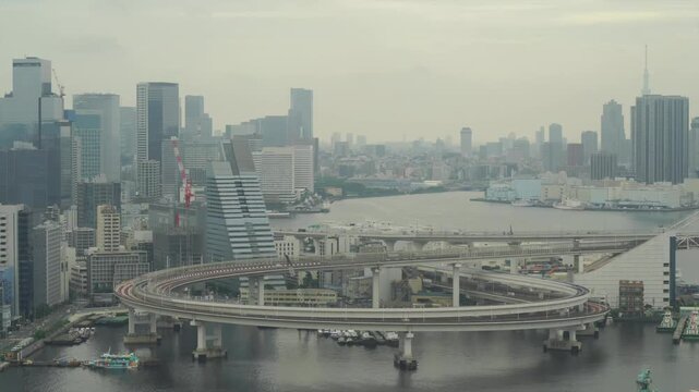 Wide timelapse view of Tokyo waterfront skyline and elevated expressway interchange over the bay on a hazy day. Modern high rises and urban infrastructure in Japan.