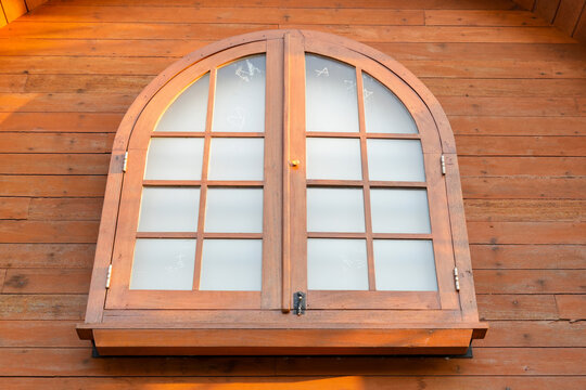 A rustic wooden dormer window on a red tiled roof with leafy trees in the background.