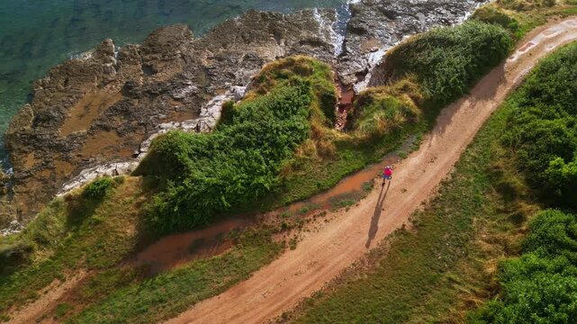 A senior adult jogs along a serene coastal path, surrounded by lush greenery and the tranquil ocean, emphasizing a commitment to a healthy lifestyle.