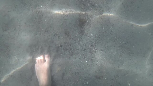 Human foot stepping on the sandy seabed of the ocean, with clear water and sunlight creating ripples