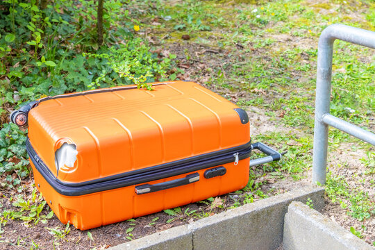 Orange suitcase with hole on ground, greenery, outdoor abandoned luggage, travel mishap, nature backdrop, discarded item, Suspicious package investigation overgrown area, Crime scene investigation