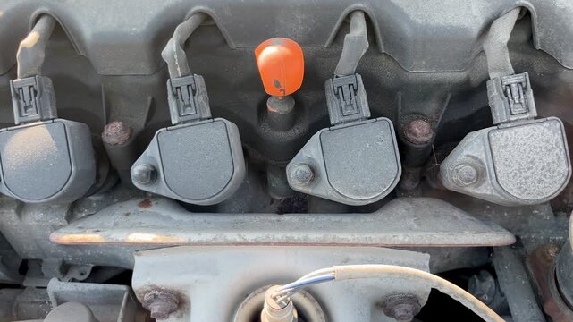 Car engine ignition coils with orange oil dipstick handle close up