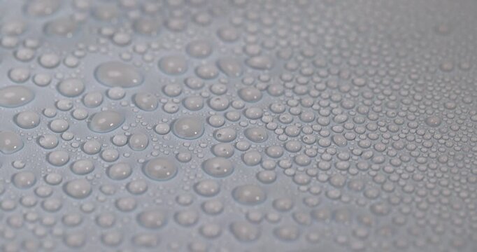 Drops lie on a blue background, transparent drops of water of different sizes on a smooth blue surface under soft light with clear details and organic texture.