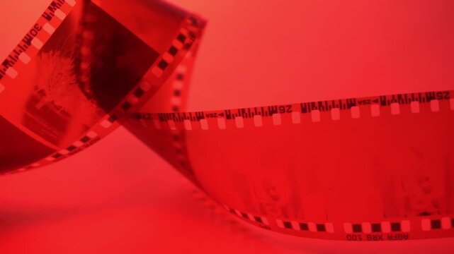 35mm negative photographic film in rotation in red room, camera darkroom. Slightly rolled film strip isolated on red background. Analog film strips. Analog photography.