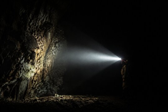A single beam of light from a helmet lamp illuminates a dark cave.