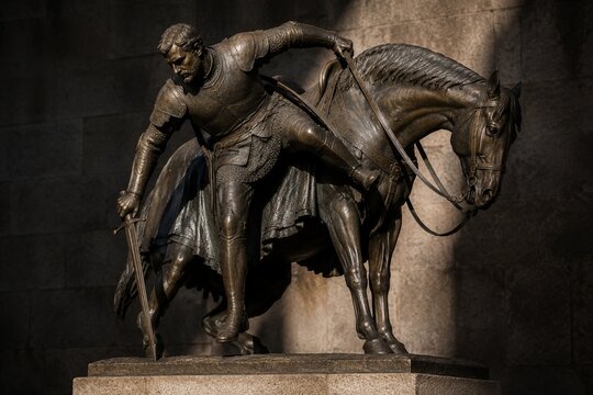 Bronze knight statue dismounting horse on stone pedestal, dramatic lighting.