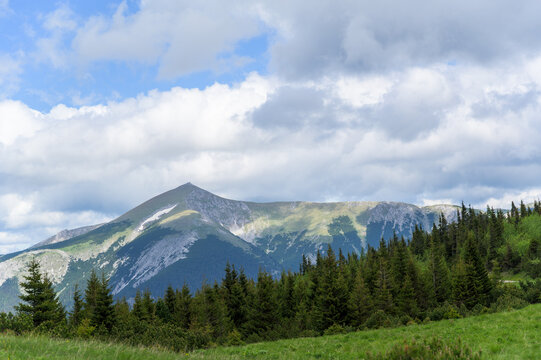 This stunning image showcases Rax Mountain in Austria with vibrant greens and rich textures under a dramatic sky filled with clouds; the foreground presents dense forests that contrast against
