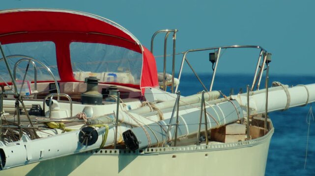 Sailboat moored at sea, carrying a disassembled mast on its deck and a red canopy, getting ready for sailing