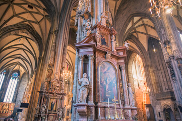 Obraz premium Vienna, Austria - June 4, 2022: Stunning interior of St. Stephen's Cathedral featuring detailed altarpiece and ornate sculptures under soft golden light illuminating rich wood tones