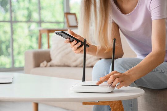 Woman setting up a wireless router with a smartphone for home internet connection and network security, the scene suggests modern technology use for residential connectivity and online activities