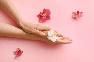 Obraz premium Female hands with delicate white orchid flower on a soft pink background, beauty and skincare
