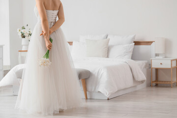 Fototapeta premium Bride in white wedding dress holding a bouquet of calla lilies behind her back in a bright bedroom