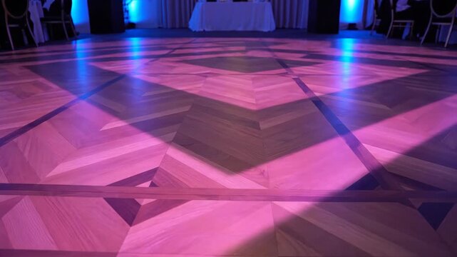 Empty wooden dance floor with purple lighting at a graduation party. Parquet surface with geometric patterns in a banquet hall. Prom or university event venue concept