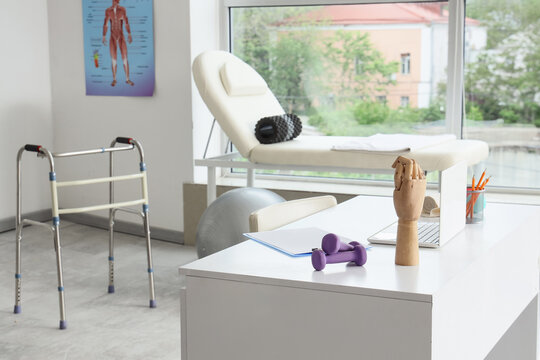 Physical therapy room with a walker, examination couch, and desk with dumbbells and a laptop