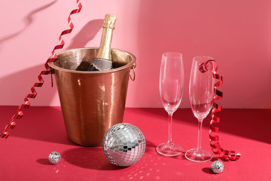 Disco balls and ice bucket with bottle of champagne on red table near pink wall