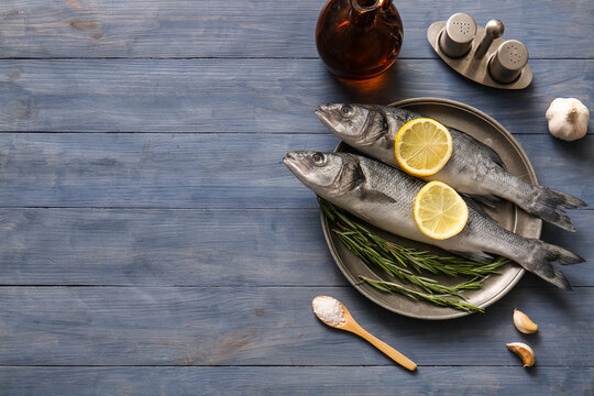 Plate with fresh raw seabass fishes and different spices on blue wooden background
