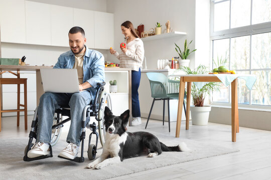 Young man in wheelchair, with laptop and dog at home