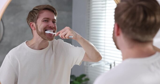 Man brushing teeth near mirror in bathroom. Oral hygiene