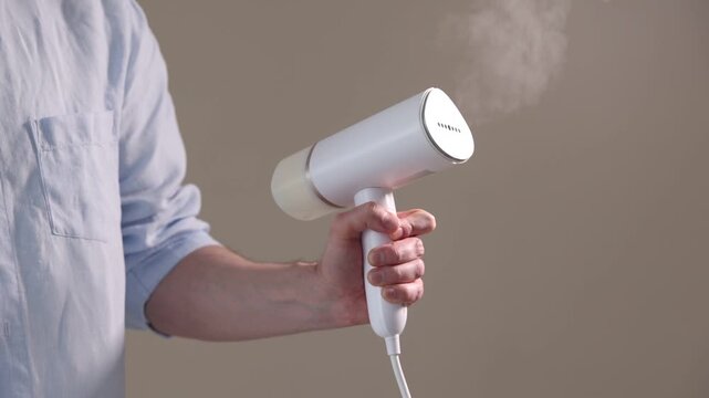Man with modern steamer on beige background, closeup. Slow motion effect