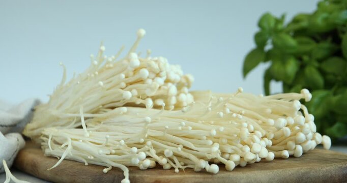 Woman putting raw enoki mushrooms on table, closeup