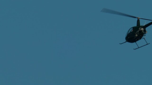 Dark green helicopter flying through a clear day sky, rotors blurring from motion. Aviation and travel concept, Antibes, France