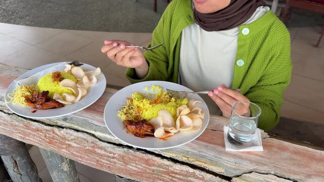 A young woman is eating yellow rice with masak habang at a seaside restaurant.