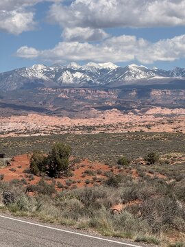 Snow capped La Sal Mountains rising above red sandstone dunes and desert scrub in Arches National Park Utah