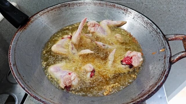 Close up of seasoned chicken wings deep frying in a pan of bubbling hot oil.
