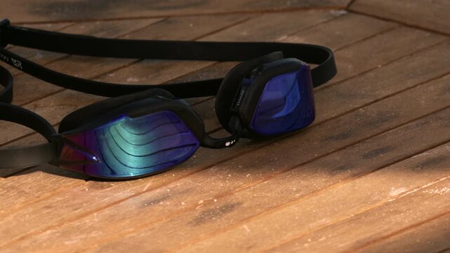 Blue and purple reflective swimming goggles lying on a rustic wooden table, catching sunlight, ready for a summer swim or vacation