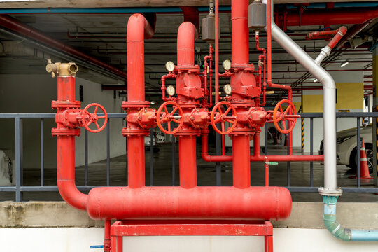 Red industrial fire protection pipes featuring valves and pressure gauges in a parking garage. Professional fire sprinkler pipeline installation for building safety and emergency water response.