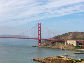 Fototapeta premium Iconic Golden Gate Bridge connecting San Francisco and Marin County, California, with its distinctive red structure spanning the strait, viewed from Sausalito with boats in a marina below a blue sky