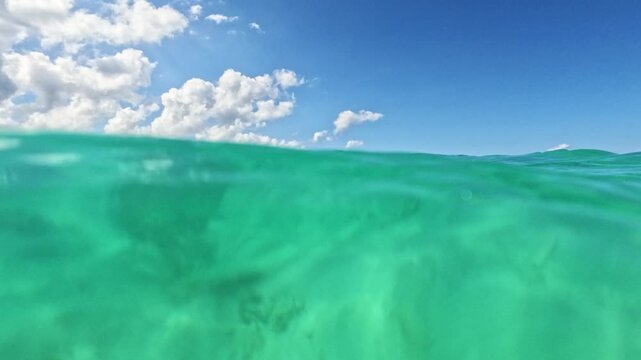 Turquoise ocean waves roll smoothly towards the shore beneath a bright blue sky filled with fluffy white clouds and distant islands on the horizon