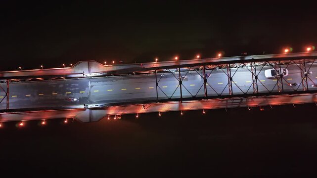 Aerial perspective of a brightly lit bridge at night, featuring vehicles in motion, highlighting the dynamic traffic and colorful illumination