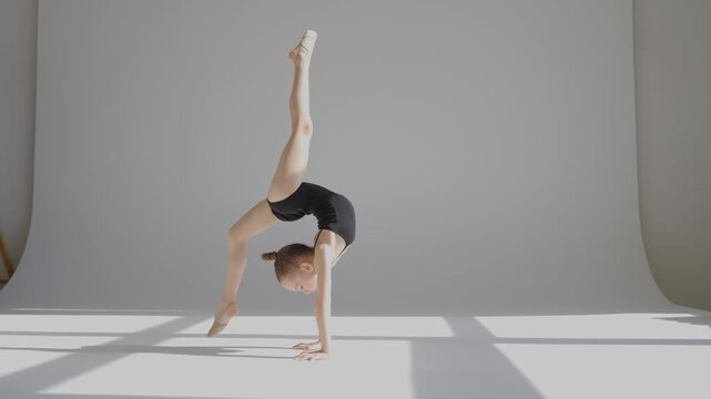 A little Caucasian girl gymnast in a black leotard does a backflip on a white background. 