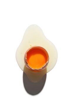 Top View of Cracked Eggshell with Bright Orange Yolk and Spilled Egg White Isolated on White Background
