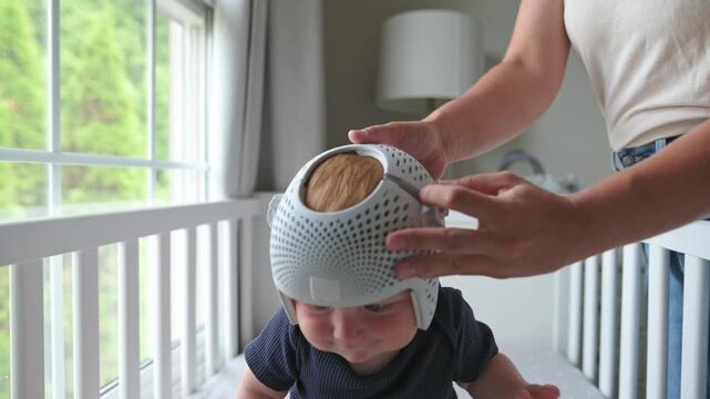 Caregiver applies a helmet for therapy on a baby, ensuring a proper fit in a well-lit nursery with soft furnishings and natural light