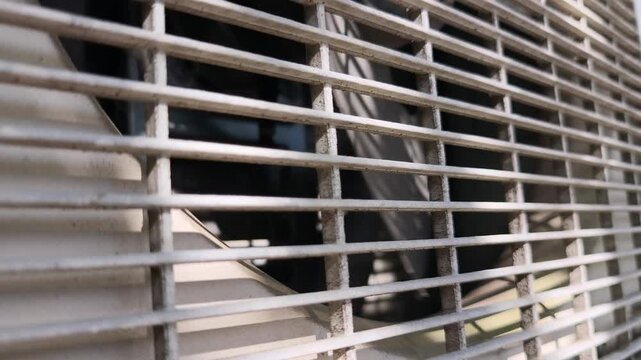 Close Up of Air Conditioner Outdoor Unit Fan Spinning Behind Metal Grille