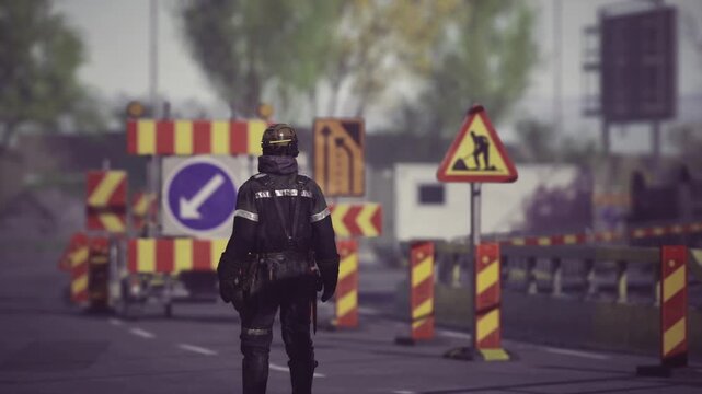 Security officer at roadside checkpoint enforcing closure, heavy protective gear and back pack visible, illuminated directional sign and striped barricade,